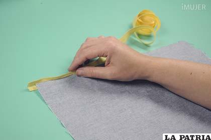 Luego, coloca la cinta amarilla sobre el borde de la tela para hacer un pequeño dobladillo.