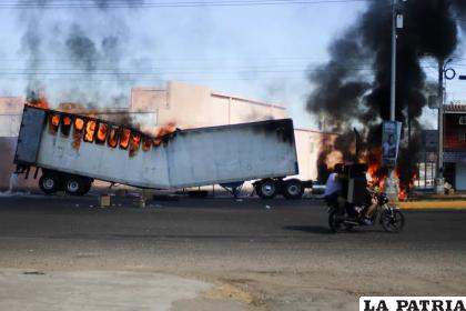 Dos hombres a bordo de una motocicleta pasan junto a un camión en llamas en las calles de Culiacán /AP Foto/Martín Urista