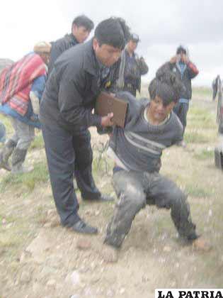 Uno de los presuntos delincuentes es ayudado por un efectivo policial tras un resbalón en el lodo