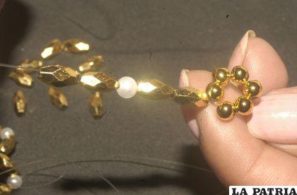 PASO 2
Insertar en cada perla 2 arroces, una perla blanca, dos arroces y cerrar el círculo con la perla dorada.
