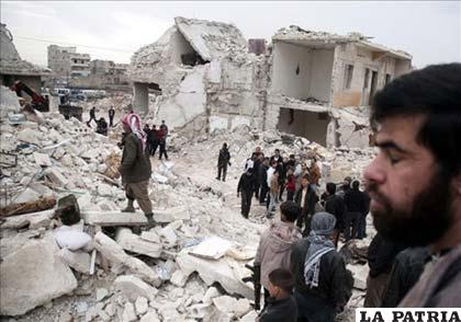 Un hombre sirio (d), observa con otras personas los daños causados en sus viviendas después del supuesto impacto de un misil
