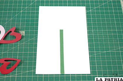 PASO 2: Cortamos un palito de papel verde y una hoja, usando la misma técnica que vimos para los pétalos. Pegamos el palito sobre una tarjeta cortada en la cartulina.