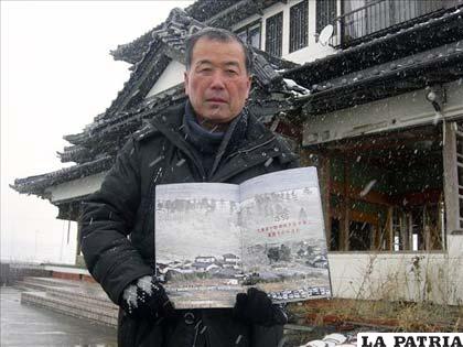 Un habitante de Natori, muestra una revista con imágenes de su casa engullida por las olas. Detrás de él aparece su vivienda ahora, una de las pocas que apenas se mantiene en pie en varios kilómetros a la redonda