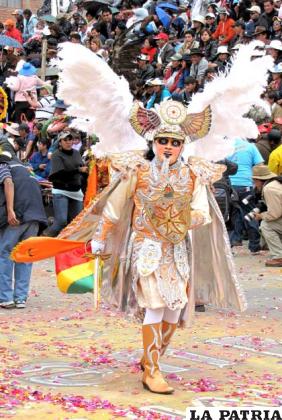 ÁNGEL: Es la principal figura de los recintos celestiales y representa el bien, dirige la tropa de diablos infernales y como abanderado de Cristo los reprime con su espada, que simboliza la justicia ante el peligro constante.
Es una figura que va delante de la tropa y con sus movimientos interpreta la lucha del bien contra el mal, la misma que termina con la derrota de los demonios, cuando los obliga a redimirse ante la Virgen del Socavón.
La característica principal de su vestimenta es que lleva un casco plateado que asemeja a un espejo, la careta que tiene facciones humanas, la cual es complementada con una peluca rizada aproximadamente hasta la altura de los hombros.
El silbato va colgado al cuello, en el pecho de la blusa se observa una cruz como símbolo de paz, en la parte posterior lleva una capilla y una capa acompañada de alas formadas con plumas.
Completan los elementos de su vestimenta en las extremidades superiores, una espada y un escudo que usa para defenderse, además un par de guantes.
También viste un buzo, encima tiene un faldón, y lleva botas decoradas con apliqués.