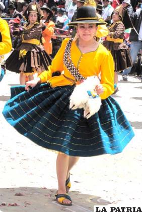 CHOLITA: La cholita, representa a la mujer campesina que arrea y pastea a las llamas. En la danza este personaje viene a englobar los bloques, portando su honda (khorawa) e imitando los movimientos del pastoreo.
Este personaje lleva en la cabeza sombrero hecho de lana de oveja adornado alrededor con greca, su cabello tiene que estar peinado en dos trenzas sujetas con tullmas, aretes y collar artesanales.
Su blusa está hecha de bayeta de la tierra.
Tiene la soga que cruza la espalda y el pecho.
En la mano derecha lleva la honda moviéndola reproduciendo el arreo de las llamas; en la mano izquierda porta una llama en miniatura.
La pollera es de bayeta de la tierra, los fustes de tela suave y abarcas de goma.