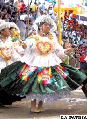 AWILA: Este personaje representa a la esposa del waphuri; baila cargando una muñeca de trapo, esto para engañar al waphuri, vigilándolo constantemente y frenando sus aventuras con las doncellas.
Lleva un sombrero cuya copa está di-
vidida en cinco partes iguales; cada una es-
tá decorada con pedrería en forma de corazones, tiene flequillos de colores vivos que se disponen alrededor del ala del sombre-
ro y que cubren parte del rostro de la promesante.
Lleva dos trenzas largas y aretes, una blusa con las mangas en forma de volados, aguayo colgado en la espalda, en el que lleva una muñeca, característica de éste personaje.
Tiene una rueca; alrededor de la cintura lleva colgadas dos ch’uspas, las que tienen flecaduras de diversos colores, en el centro de las bolsitas una cruz.
La longitud de la pollera varía. Sus zapatos son de taco bajo.
Toda la vestimenta es colorida, especialmente se eligen colores chillones, como los verdes, celestes, fucsias, plateados, dorados, entre otros, con combinados de mucho contraste.