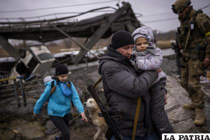 El miliciano local Valery, de 37 años, lleva a una niña en brazos mientras ayuda a una familia que huye junto a un puente destruido por artillería /Foto AP /Emilio Morenatti