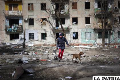 Un hombre camina con su perro cerca de un edificio dañado por proyectiles a las afueras de Mariúpol, Ucrania /AP Foto/Alexei Alexandrov