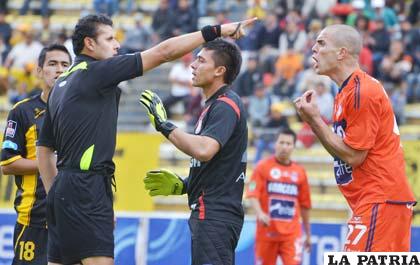 El árbitro Gery Vargas amonesta al defensor Martín Aguirre de Universitario. Al centro aparece al golero Jorge Ruth tratando de calmar los ánimos