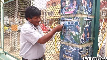 El gobernador electo sacando con mucho esfuerzo algunos afiches suyos pegados en un muro
