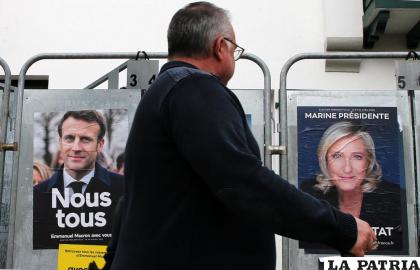 Un hombre pasa frente a dos murales del presidente francés Emmanuel Macron, de centro, y la candidata Marine Le Pen /AP Foto/Bob Edme