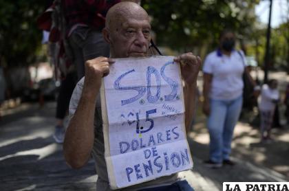 Carlos Blanco, de 84 años, supervisor de ambulancias retirado, sostiene un cartel que anuncia el pago mensual de su pensión de $1.50 dólares 
/Foto AP/Ariana Cubillos, Archivo
