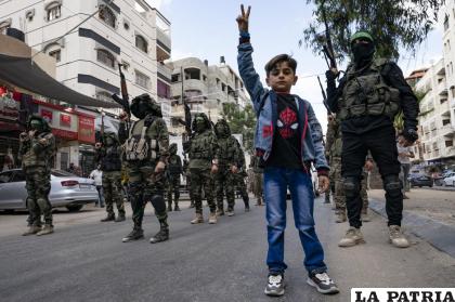 Un niño hace la señal de la victoria frente a milicianos de Hamas haciendo una pausa durante un desfile por las calles /AP Foto/John Minchillo