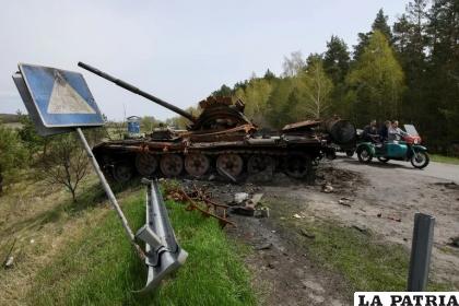 La gente pasa en motocicleta por los escombros de la maquinaria militar rusa destruida durante la invasión rusa de Ucrania, en el pueblo de Rusaniv, región de Kiev /REUTERS/Vladyslav Musiienko