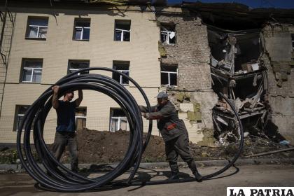 Trabajadores municipales preparan un tubo para restaurar el suministro de agua frente a un edificio dañado por un ataque ruso en Bahmut, Ucrania /AP Foto/Evgeniy Maloletka