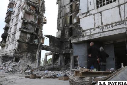 Residentes, parados junto a edificios gravemente dañados por los intensos combates en Mariúpol /AP Foto