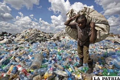 Un hombre camina sobre una montaña de botellas de plástico mientras carga un saco lleno de ellas en Nairobi, Kenia. /Ben Curtis /Associated Press