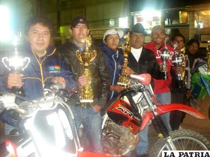 Pilotos que intervendrán en la competencia con los trofeos que se entregarán a los ganadores