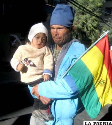 Indígena junto a su hijo porta el emblema patrio al ingreso a la sede de gobierno
