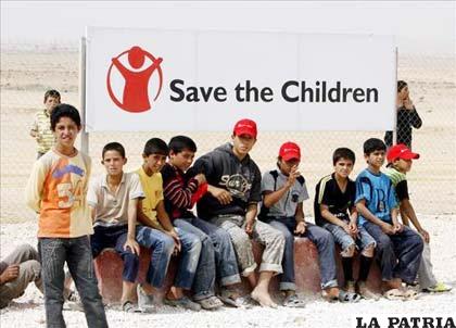 Niños refugiados sirios ante un cartel de la ONG “Save the children”