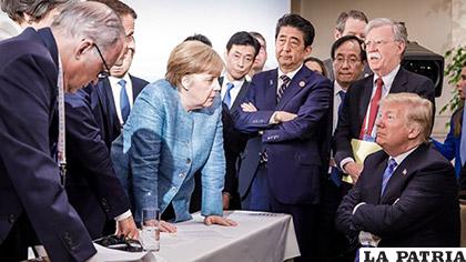 Trump está sentado con los brazos cruzados y Merkel de pie, con el presidente francés Emmanuel Macron /RPP