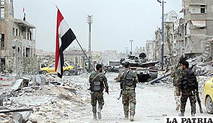 Una patrulla de soldados del Ejército sirio sujeta una bandera siria en el campamento de Yarmouk, al sur de Damasco /EFE