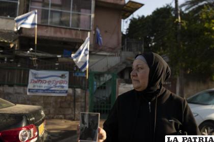 Maryam Ghawi, una mujer palestina, posa con una foto de la casa detrás suyo, en la que alguna vez vivió /AP Photo/Maya Alleruzzo)