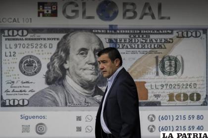 Un hombre camina frente a una casa de cambio con una imagen de un billete de 100 dólares, en Bogotá, Colombia. /AP Foto /Ivan Valencia