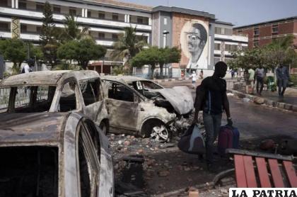 Con sus pertenencias, un estudiante pasa junto a autos quemados al salir de la Universidad Cheikh Anta Diop /AP