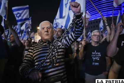 Numerosas personas, entre ellas una disfrazada del primer ministro israelí Benjamin Netanyahu encadenado, protestan contra los planes del gobierno /AP Foto/Tsafrir Abayov