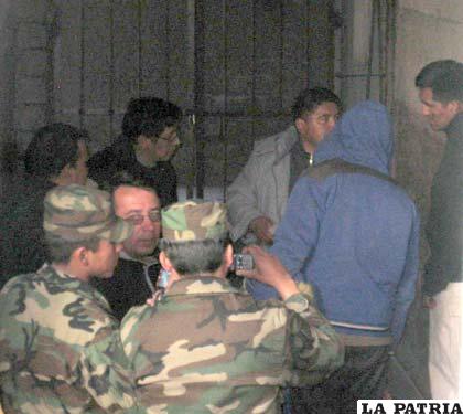 En las puertas de las celdas de la Felcc, autoridades militares y de la Fiscalía resguardan a dos aprehendidos en el operativo