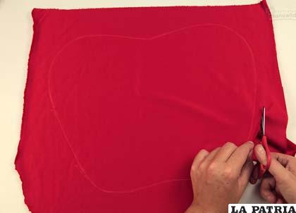 PASO 2
Toma la tijera y corta la tela siguiendo la línea que habías trazado en el paso anterior, pero procura dejar un espacio de más o menos 2 centímetros para la costura.
Repite los pasos anteriores para obtener una figura igual a la que acabas de hacer también en tela roja.