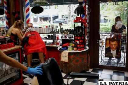Un peluquero con una máscara protectora corta el pelo de un hombre en una peluquería de Miami /infobae.com