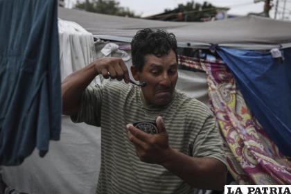 El migrante hondureño Christian Fragoso sostiene un espejo en una mano mientras se afeita la cara en un campamento de migrantes /AP Photo/Emilio Espejel