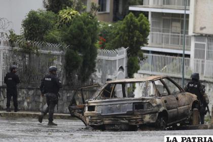 Miembros de la Unidad Especial de Operaciones Tácticas pasan junto a un vehículo que se incendió en el barrio Cota 905, en Caracas /AP Foto/Ariana Cubillos