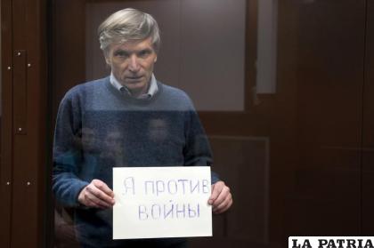 Alexei Gorinov sostiene un cartel que lee “Estoy en contra de la guerra” mientras está de pie detrás del vidrio del banquillo de los acusados /AP Foto /Alexander Zemlianichenko, Archivo