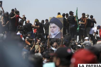 Un manifestante sostiene un cartel con la imagen del clérigo chií Muqtada al-Sadr /AP Foto/Anmar Khalil