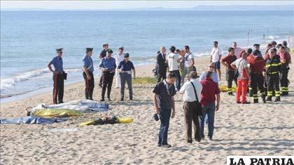 Agentes de la Guardia Costera, de la Policía y los Carabineros permanecen junto a los cuerpos de los inmigrantes muertos en la playa cerca de Catania
