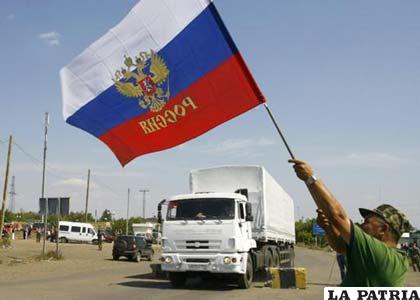 Habitante local ondea bandera de Rusia mientras camiones del convoy humanitario ruso cruzan la frontera ucraniana