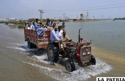 Varias personas viajan en la caja de un camión remolcada por un tractor en un área inundada de Sohbatpur /AP Foto /Zahid Hussain
