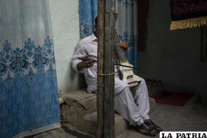Un hombre tapado por un poste para ocultar su identidad posa con su dilruba en Kabul /AP PHOTO / Bernat Armangue