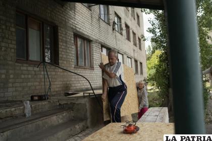 Henadii Sydorenko carga con una tabla de madera para cubrir las ventanas de los departamentos dañados por un ataque ruso /AP Foto /Leo Correa