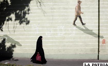 Imagen de archivo de una mujer iraní con velo que pasa junto a una pared con un soldado iraní pintado en ella en una calle de Teherán /EFE /Abedin Taherkenareh