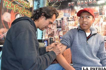 El artista realiza el tatuaje temporal en el brazo de un visitante de la feria
