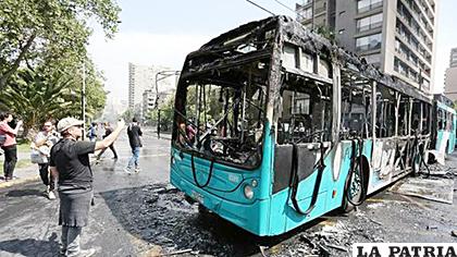 Fotografía de un autobús incinerado durante las protestas contra el incremento del precio en los billetes del metro, este sábado en Santiago (Chile) /EFE