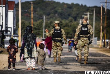 Policías militares caminan frente a unos refugiados afganos en la base del ejército estadounidense Fort McCoy /Barbara Davidson /Pool Photo víaAP