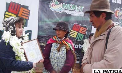 Janette Albiz, del Viceministerio de Tierras, entrega certificado catastral a uno de los beneficiarios