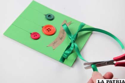 PASO 6
Elige una cinta verde que no sea demasiado gruesa y arma una moña para pegar en la parte interior de la tarjeta navideña. Antes de escribir en el interior, corta los excesos de cinta que hayan quedado.