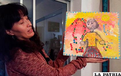 La artista Sulma Montero, sostiene un cuadro pintado por una niña