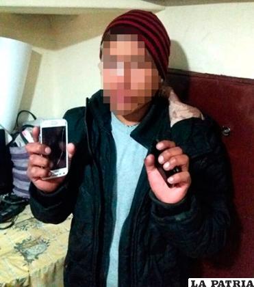 El muchacho muestra dos de los celulares que se le encontraron